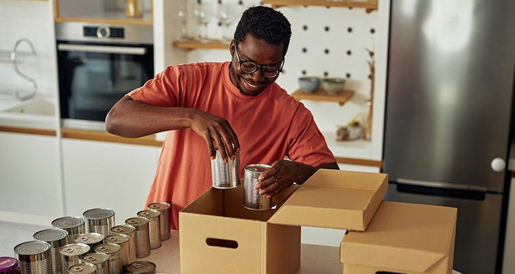 CIG-Impact Young man packs cans of food into boxes in a kitchen