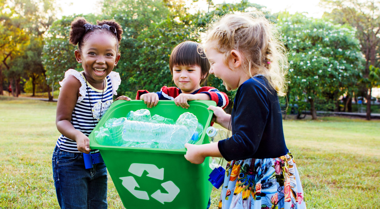 Three little kids hold up a recycling bin full of plastic