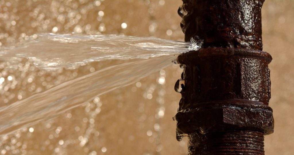 Closeup of a brown pipe with water bursting from one of the seams