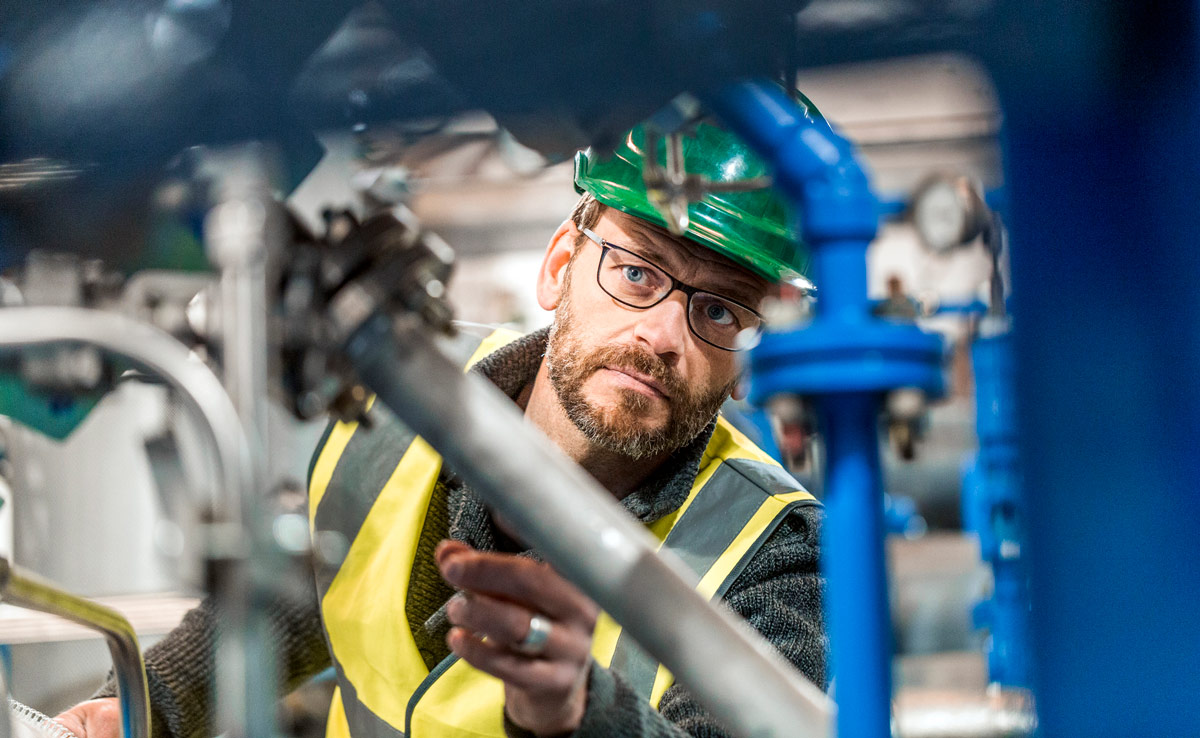 A man wearing a safety hat and vest inspects a series of pipes