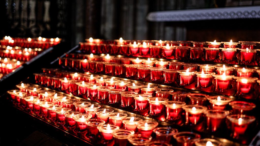 Rows of small tea light candles lit in a dark setting