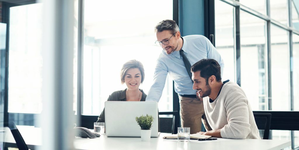 Three colleagues in a brightly lit office looking at a laptop