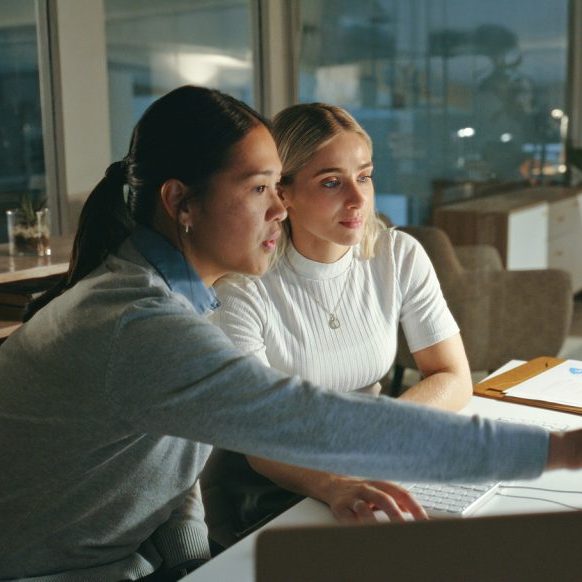 Two young women looking at a computer screen in an office in the evening