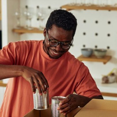 A young Black man packs boxes with canned goods in a kitchen