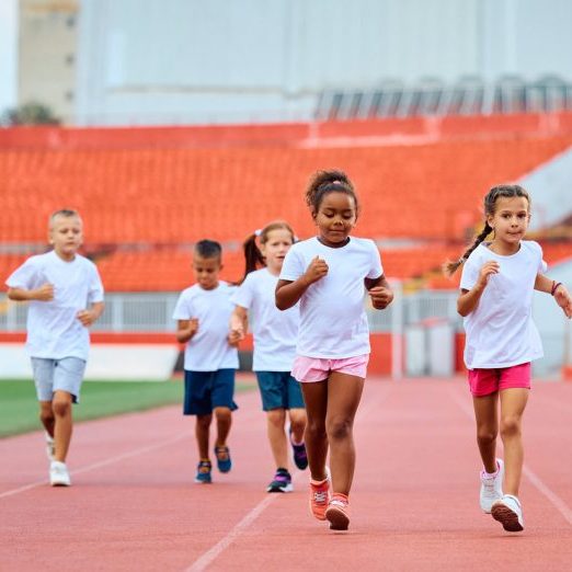 Group of young students running a track, with their teacher in the background