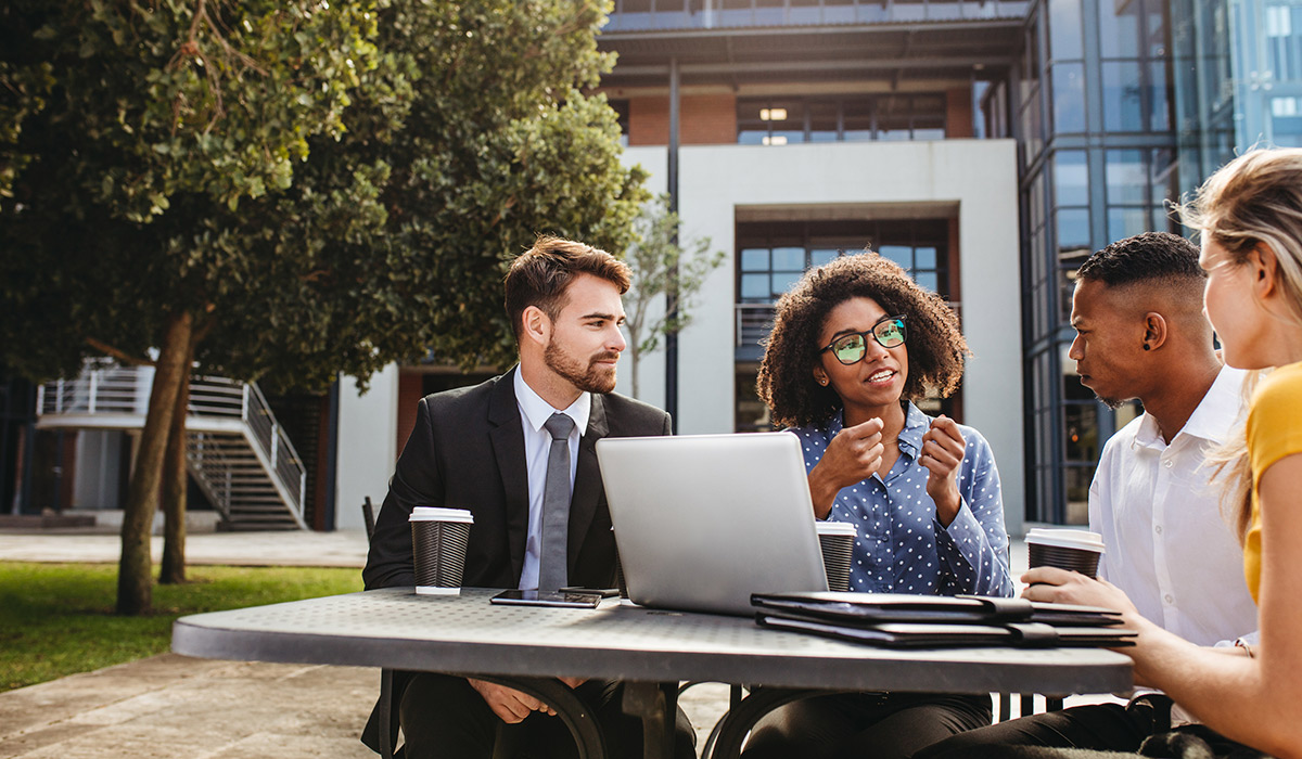 Diverse group of young coworkers sits at a table outside and has a meeting