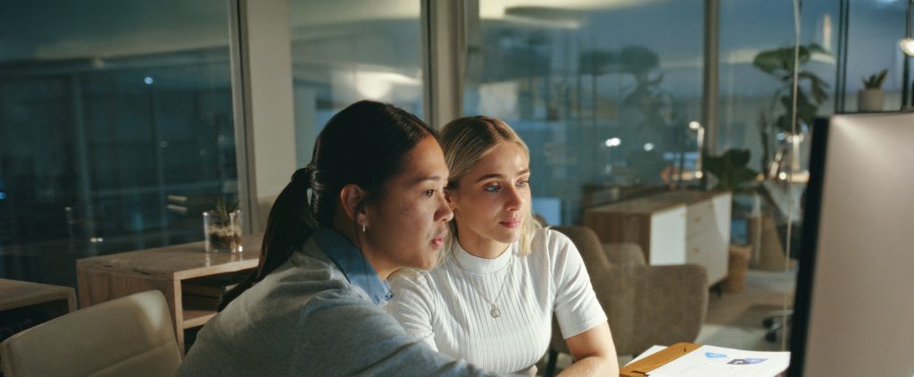 Two young women looking at a computer screen in an office in the evening