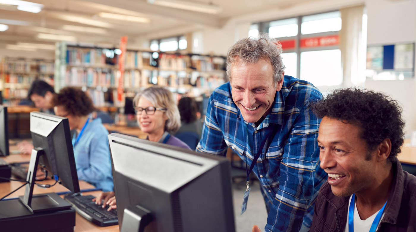 education-01 Older man helps a young man on a computer at a library