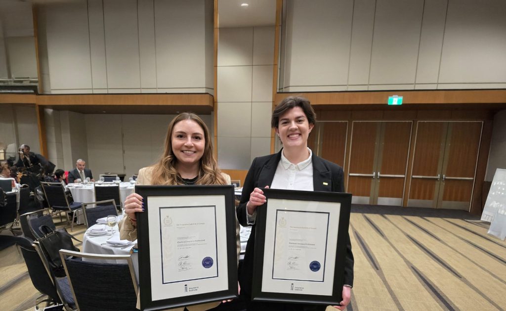 Two young employees holding framed awards