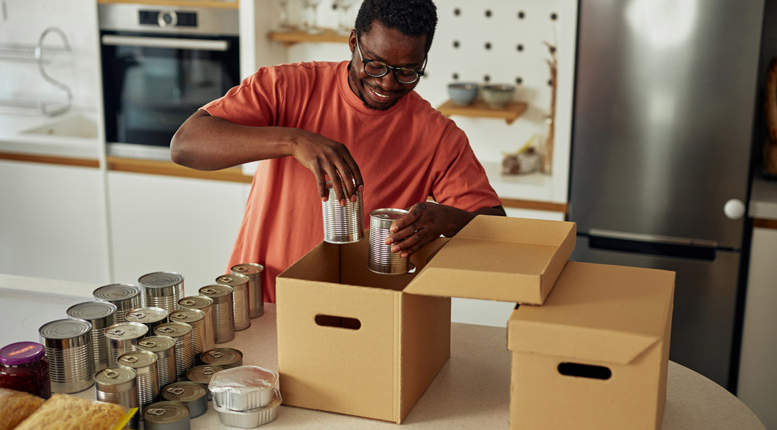 A young Black man packs boxes with canned goods in a kitchen