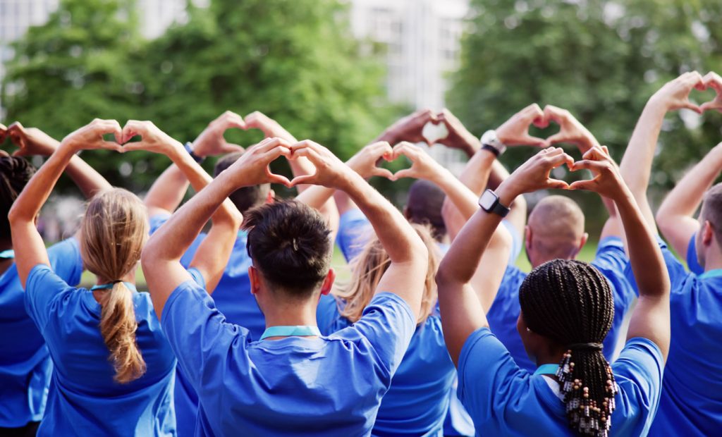 View of the backs of a group of people wearing matching blue shirts using their hands to create heart shapes above their heads