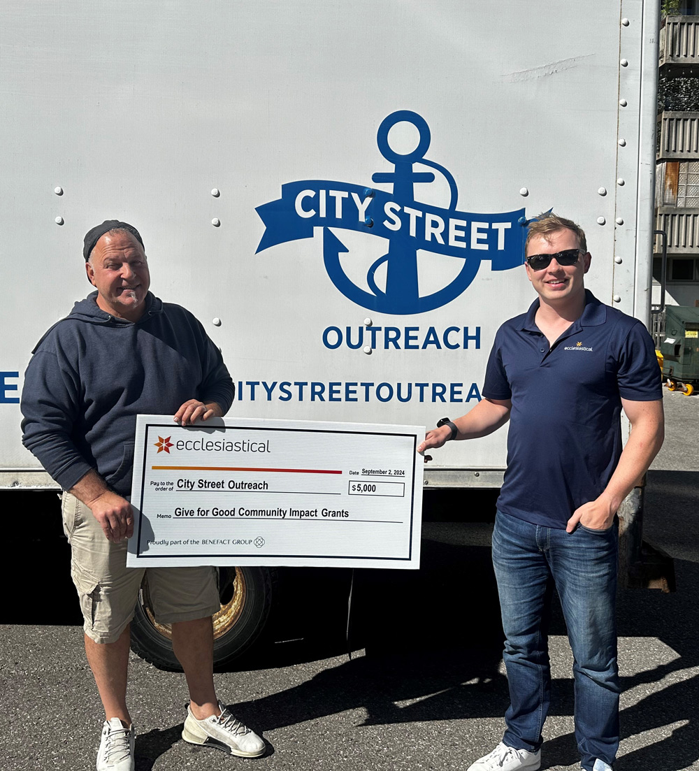 Two peopl standing in front of a truck with a City Street logo, holding a giant cheque