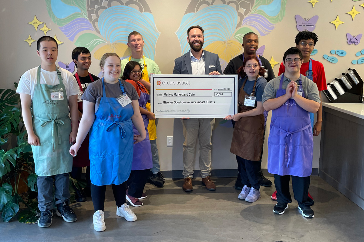 Group of cafe employees smiling and one person is holding a giant novelty cheque