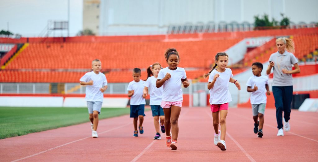 Group of young students running a track, with their teacher in the background