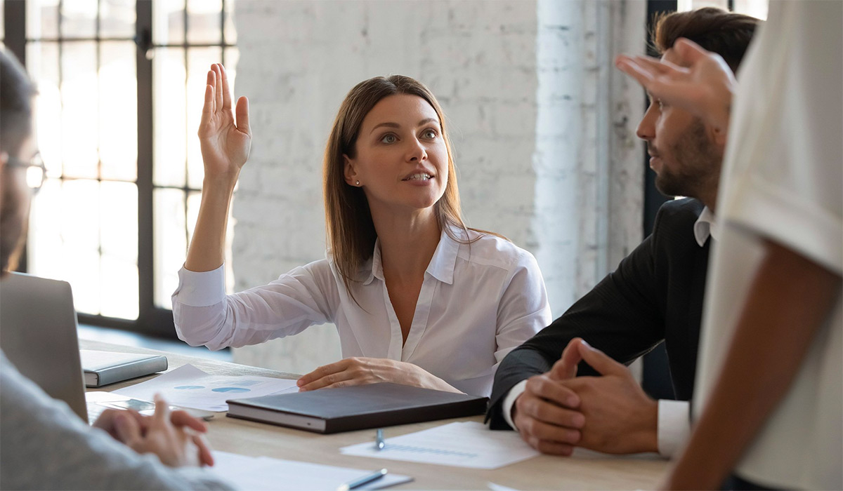 Young professional woman at a table with coworkers raising her hand