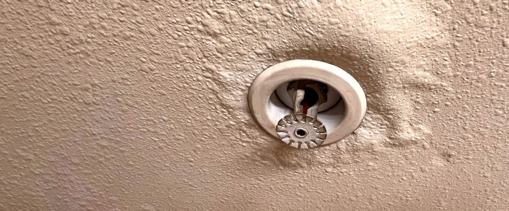 Close up of a sprinkler in a ceiling with visible water damage