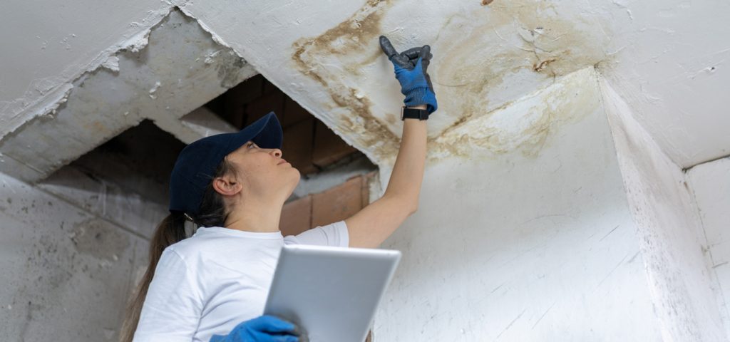 A person inspects a ceiling that has water damage